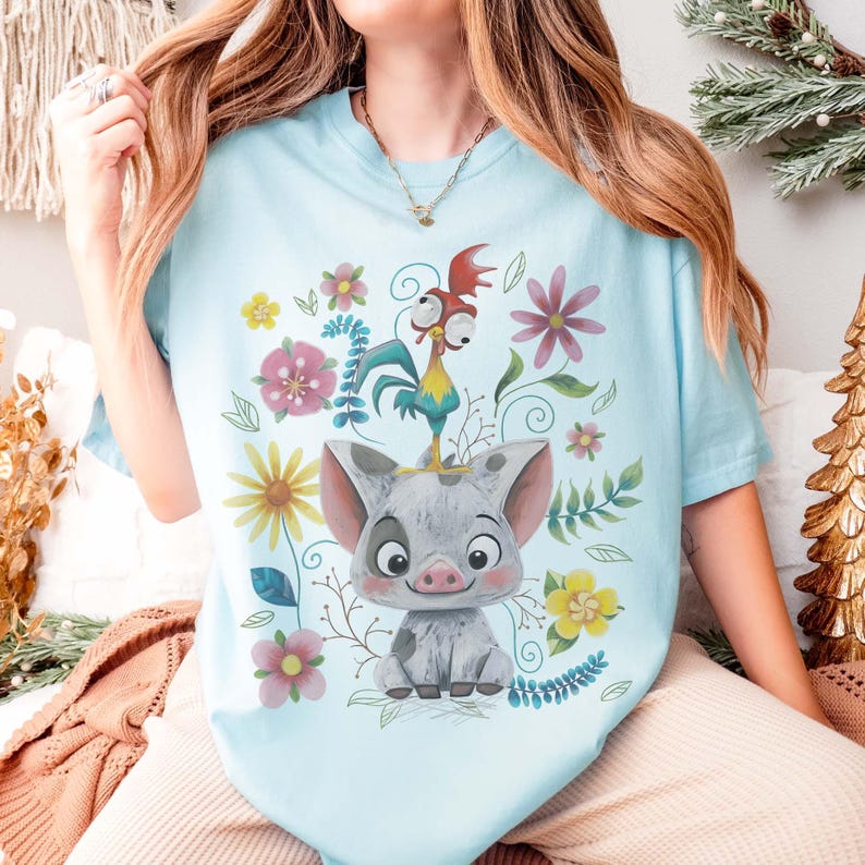 Puede incluir: Camiseta azul claro con un dise&ntilde;o de cerdo y gallo de dibujos animados, rodeada de flores y hojas coloridas. La ilustraci&oacute;n es juguetona y brillante, ideal para los fan&aacute;ticos de las pel&iacute;culas de animaci&oacute;n.