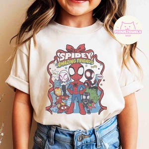Puede incluir: Camiseta color crema con un gr&aacute;fico colorido de Spider-Man y otros personajes. El dise&ntilde;o incluye a Iron Man, Hulk y otros h&eacute;roes, con el texto "Spidey Amazing Friends".