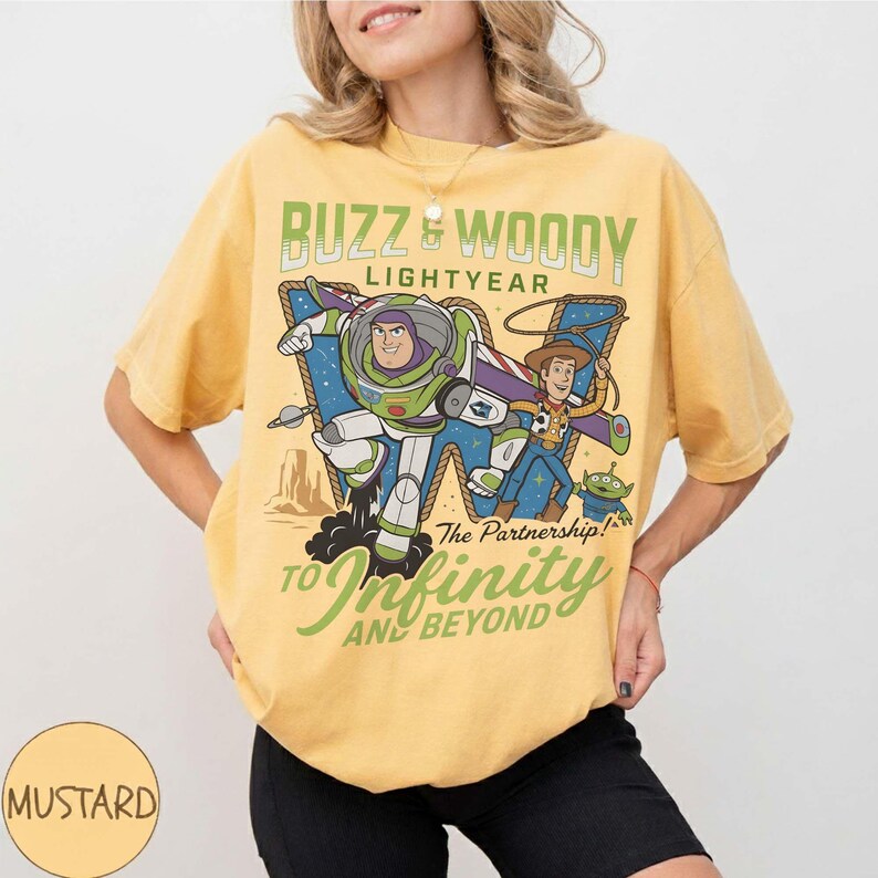 Może przedstawiać: Musztardowa koszulka z Buzzem Astralem, Chudym i obcym z Toy Story. Grafika zawiera tekst "Buzz & Woody Lightyear" i "To Infinity and Beyond". Koszulka ma luźny kr&oacute;j.