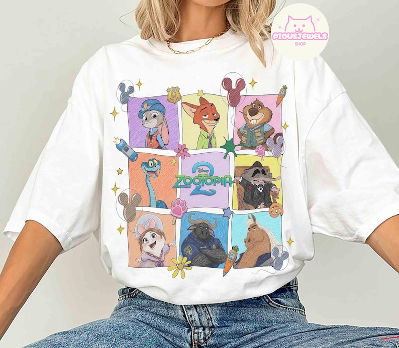 May include: White t-shirt featuring a colorful grid of Zootopia 2 characters. The design includes Judy Hopps, Nick Wilde, and other characters in a cartoon style. The shirt has a crew neck and short sleeves.