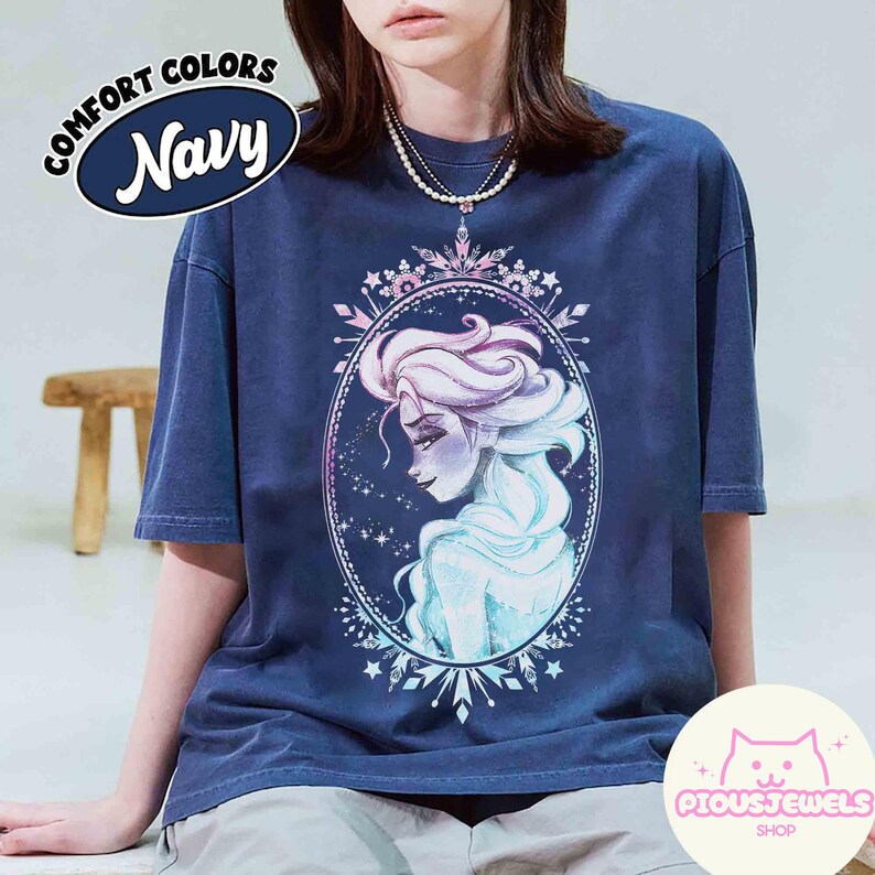 May include: Navy blue t-shirt with a watercolor illustration of a woman with long, flowing hair inside an oval frame. The shirt has the text "COMFORT COLORS Navy" on the upper left and the shop logo "PIOUSJEWELS SHOP" on the lower right.
