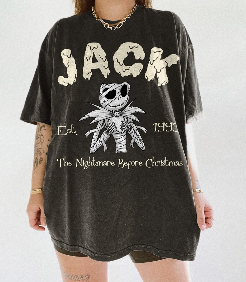 K&ouml;nnte beinhalten: Dunkelgraues T-Shirt mit dem Wort "JACK" in tropfender Schrift &uuml;ber einer Illustration von Jack Skellington aus "The Nightmare Before Christmas". Das Shirt enth&auml;lt auch den Text "Est. 1993" und "The Nightmare Before Christmas."