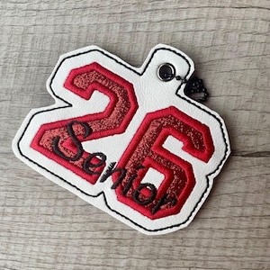 May include: White felt keychain with a red glitter number 26 and the word "Senior" in red embroidery.