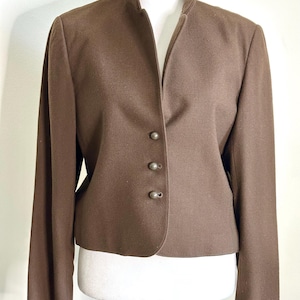 May include: A brown blazer with a mandarin collar and a single button fastening. The blazer has a fitted silhouette and long sleeves.