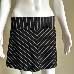 May include: A black and white striped skirt. The skirt features a wide waistband with vertical stripes and a chevron pattern on the skirt. The skirt is displayed on a mannequin.