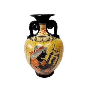 Puede incluir: Un jarrón decorativo de cerámica con borde y asas negros. El jarrón presenta un fondo amarillo con una ilustración en negro y rojo de una persona tocando un instrumento de cuerda. El jarrón tiene un diseño griego clásico.