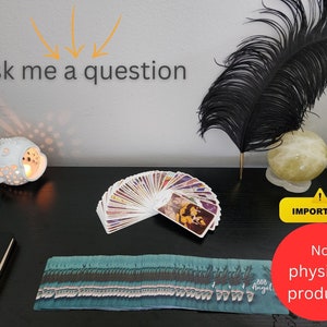 May include: A black table with a white ceramic fish candle holder, a deck of tarot cards, a black feather, a yellow crystal ball, and a sign that says "Ask me a question".