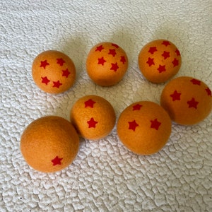 Könnte beinhalten: Sieben orangefarbene Filzkugeln mit roten Sternen darauf. Die Kugeln sind in einem Halbkreis auf einer weißen Oberfläche angeordnet.