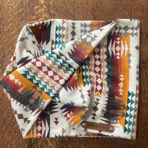 May include: Cream-colored headband with a Southwestern geometric pattern in shades of teal, orange, brown, and gray. The headband has a leather tag that reads "MERLE & TRT".