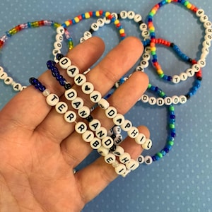 May include: A collection of colorful beaded bracelets with names spelled out on them. The names include "Dan", "Terrib", "And", "Phil", "Dyd", "Door", "Titso", and "Tfordnp".