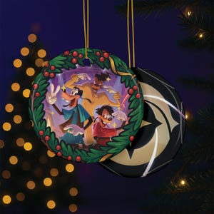 May include: A round Christmas ornament featuring a cartoon image of Goofy and his son Max, surrounded by a wreath of green leaves and red berries. The reverse side is black with a gold starburst design. A gold string is attached for hanging.