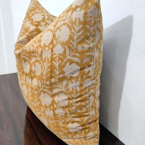 May include: A mustard yellow cushion with a white floral pattern. The cushion is made of a soft, cotton fabric and has a subtle sheen.