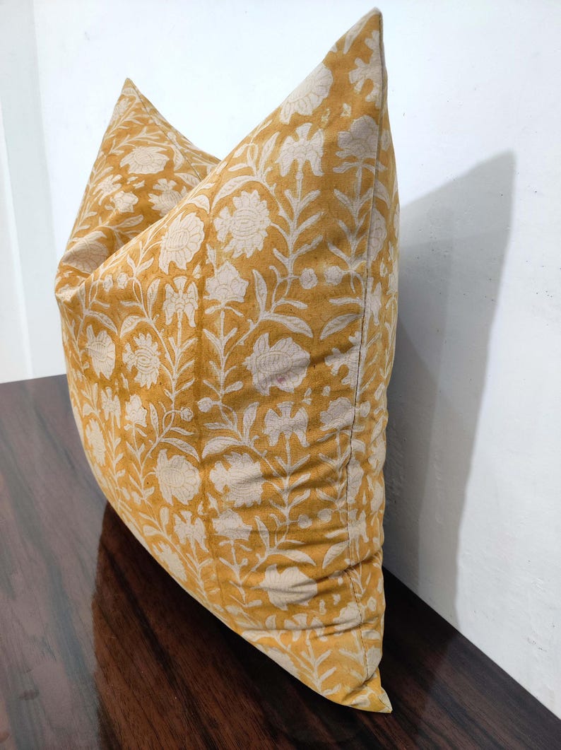 May include: A mustard yellow cushion with a white floral pattern. The cushion is made of a soft, cotton fabric and has a subtle sheen.
