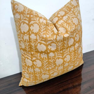 May include: A mustard yellow cushion with a white floral pattern. The cushion is made of a soft, cotton fabric and has a subtle sheen.