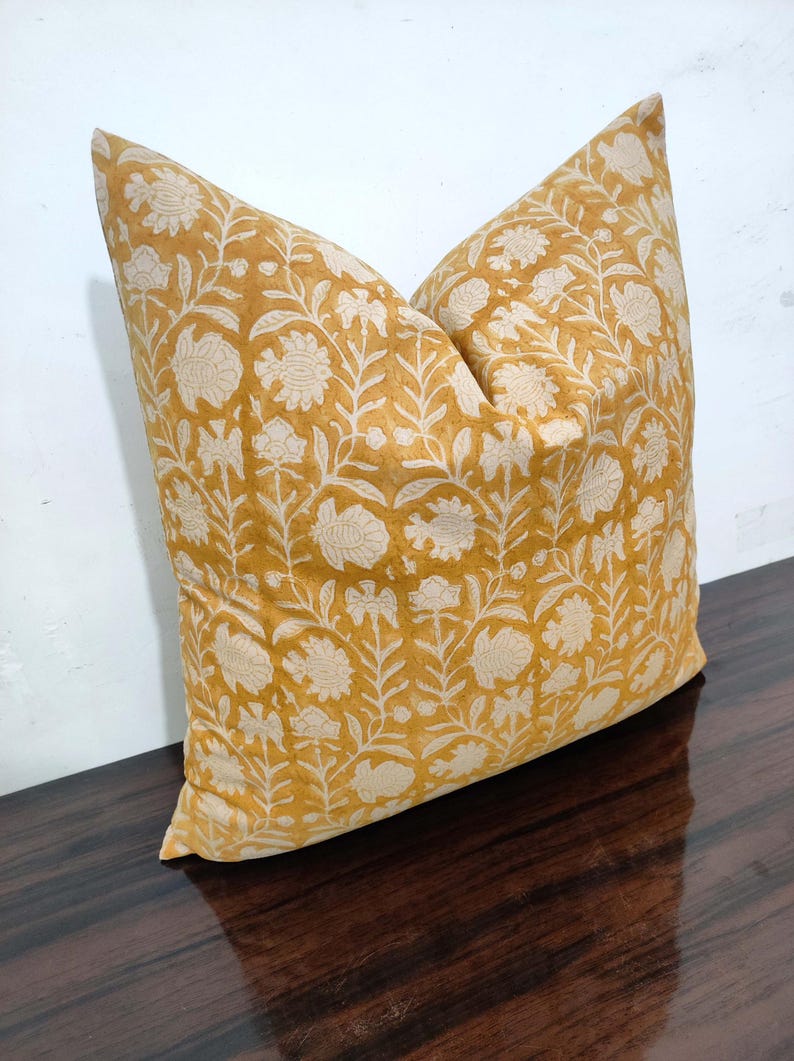 May include: A mustard yellow cushion with a white floral pattern. The cushion is made of a soft, cotton fabric and has a subtle sheen.