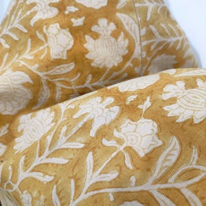 May include: A close-up of a yellow fabric with a white floral pattern. The fabric is soft and has a subtle sheen.