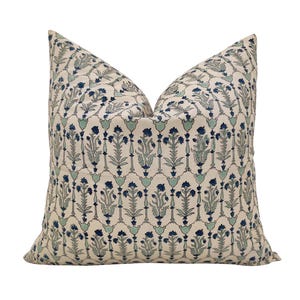 Puede incluir: Un cojín decorativo con un fondo crema y un patrón floral repetido en tonos azules y turquesas. El cojín tiene una forma clásica y está diseñado para la decoración del hogar.