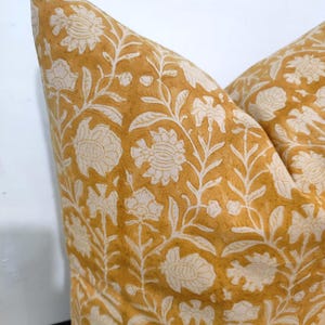 May include: A mustard yellow throw pillow with a white floral pattern. The pillow is made of a soft, cotton fabric and has a subtle, vintage look.