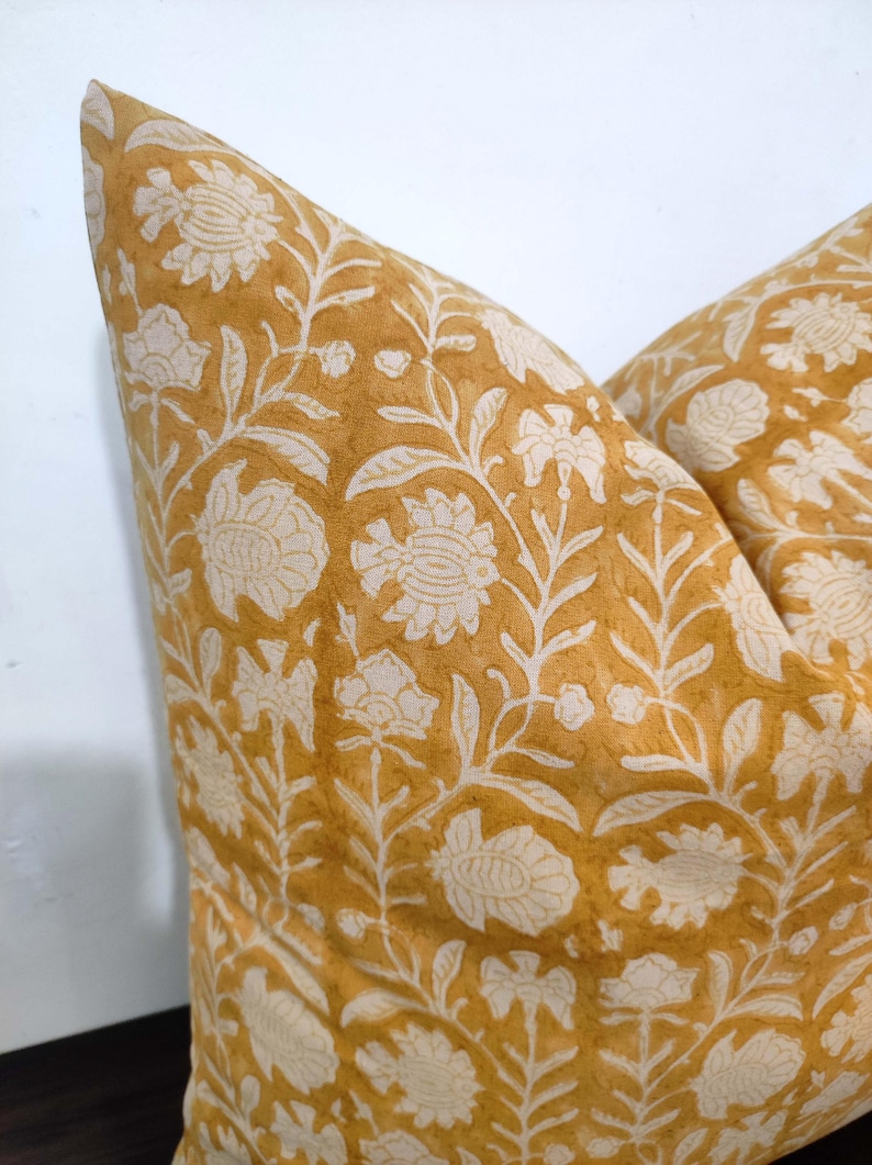 May include: A mustard yellow throw pillow with a white floral pattern. The pillow is made of a soft, cotton fabric and has a subtle, vintage look.