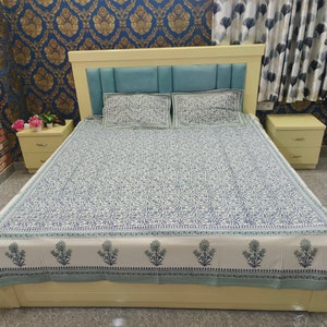 Può includere: Un lenzuolo da letto bianco e blu con motivo e un bordo verde. Il lenzuolo è su un letto con una testiera blu chiaro e due cuscini abbinati.
