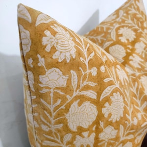 May include: A mustard yellow pillow cover with a white floral pattern. The pillow cover is made of a soft, linen fabric.