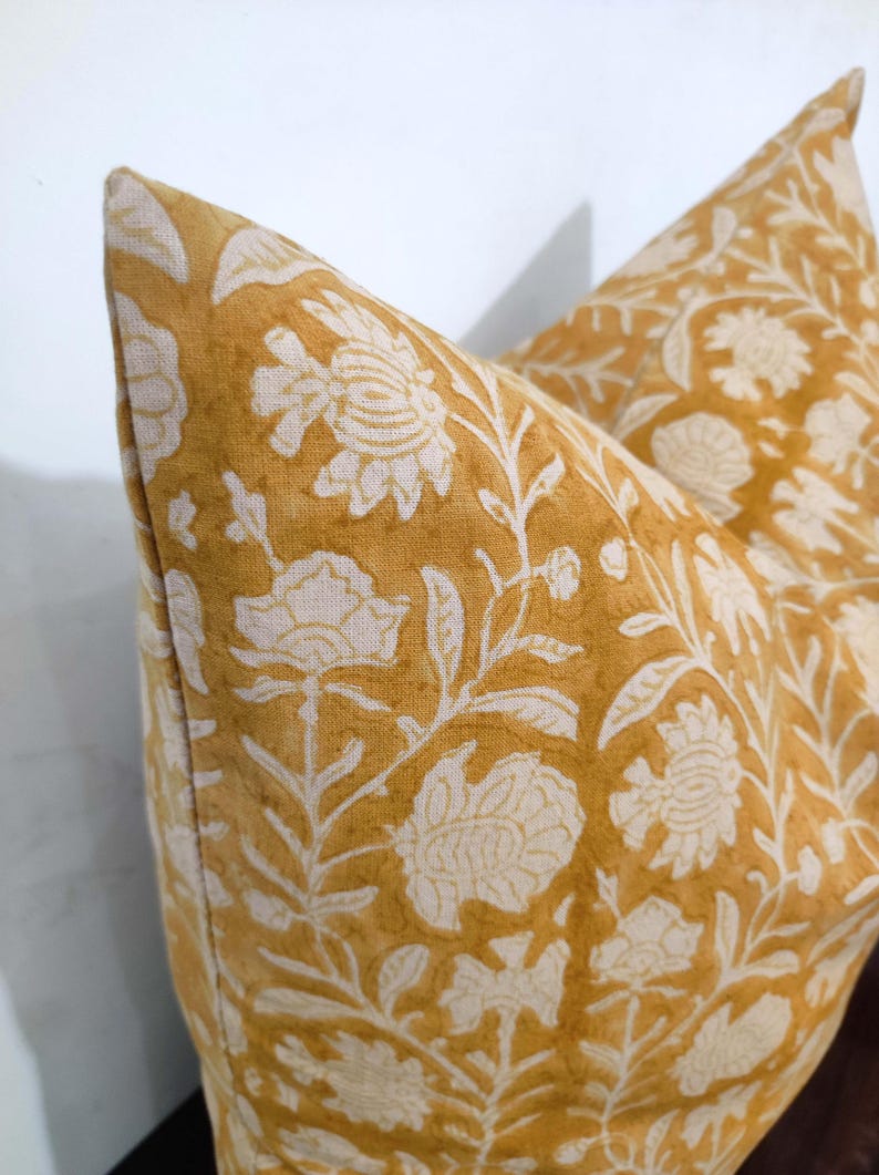 May include: A mustard yellow pillow cover with a white floral pattern. The pillow cover is made of a soft, linen fabric.
