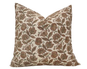 May include: A square cushion with a floral pattern. The cushion has a cream background with a repeating design of brown and green flowers and leaves. A soft, decorative item for the home.