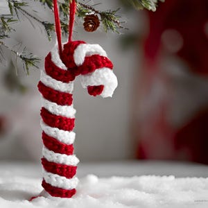 May include: A red and white crocheted candy cane ornament hanging from a Christmas tree.