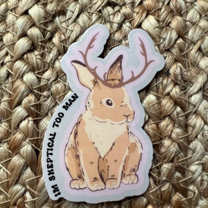 May include: A sticker featuring a cartoon rabbit with antlers and the text "I'm skeptical too man". The rabbit is brown and white and has a light pink background.