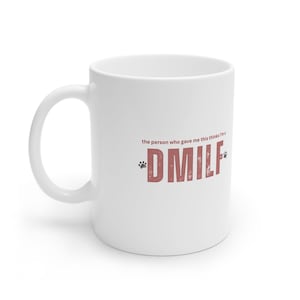 May include: White ceramic coffee mug with the text "the person who gave me this thinks I'm a *DMILF*" in pink with paw prints on either side of the text.