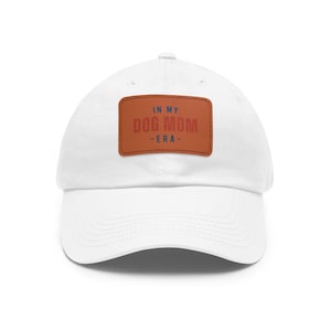 Puede incluir: Gorra de béisbol blanca con un parche de cuero marrón que dice "In My Dog Mom Era" en letras rojas y azules.