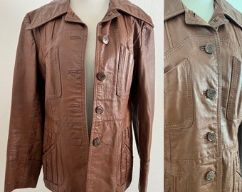 May include: A brown leather jacket with a collared neckline, button closure, and multiple pockets. The jacket has a fitted silhouette and a slightly flared hem.
