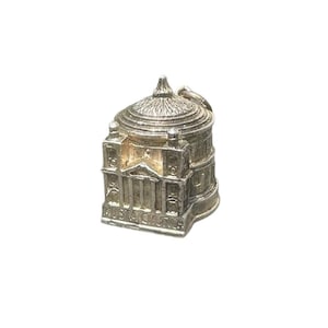 May include: A silver-toned charm in the shape of a domed building with columns and architectural details. The charm has a small loop at the top for attachment. The building charm is set against a white background.