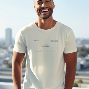 May include: A cream-colored short-sleeve t-shirt featuring black printed text that mimics a business card. The text reads Pierce & Pierce, Patrick Bateman, Vice President, and includes a New York address and phone number 212 555 6342.