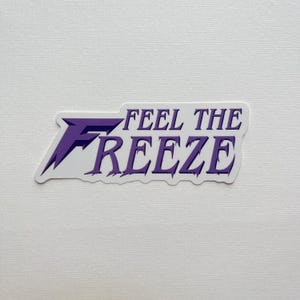 May include: A white sticker with the text "FEEL THE FREEZE" in purple. The sticker has a purple and white design with a jagged edge.