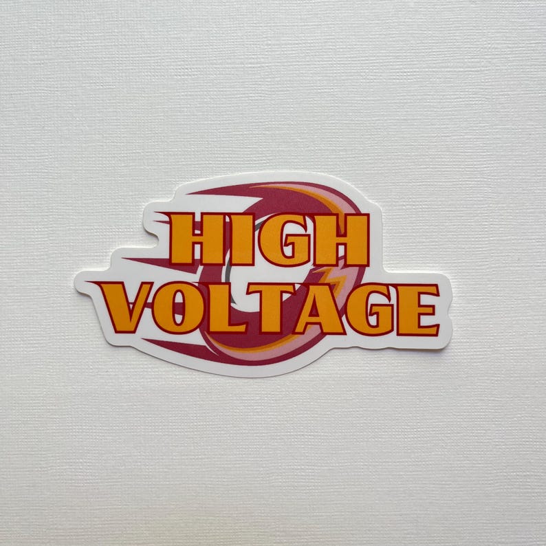 May include: A white sticker with the words "HIGH VOLTAGE" in orange block letters. The text is outlined in red and set against a stylized flame design in red, orange, and white.