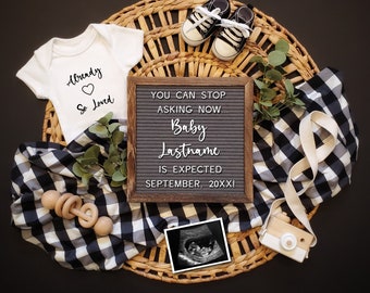 May include: A black and white checkered fabric with a wooden woven tray, a letter board with the text "YOU CAN STOP ASKING NOW... Baby Lastname IS EXPECTED SEPTEMBER, 20XX!" and a white onesie with the text "Already So Loved" on it. There is also a pair of baby shoes, a wooden rattle, a small ultrasound image, and a small camera.