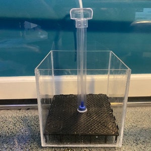 May include: A clear, rectangular aquarium filter with a black, textured base. A clear tube extends from the base, connected to a clear plastic top. The filter is designed for aquatic environments.