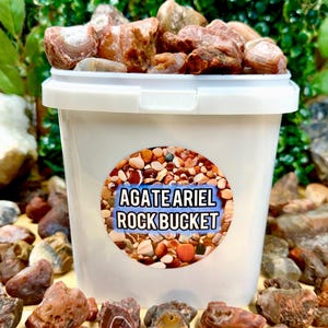 May include: A white bucket filled with agate rocks. The bucket has a sticker that says "Agate Ariel Rock Bucket".