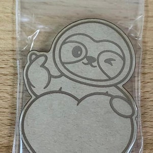 May include: A brown paper cutout of a sloth with a heart-shaped body. The sloth is winking and giving a thumbs up.