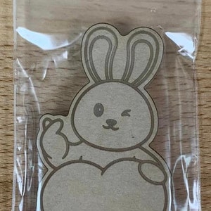 May include: A brown paper cutout of a bunny rabbit holding a heart. The bunny is winking and has a simple, cartoon-like design.