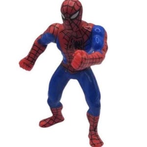 May include: A red, blue, and black Spider-Man action figure in a dynamic pose. The figure has a red mask and suit with a web pattern, blue accents, and a black spider emblem on the chest. The figure is standing with one arm raised.