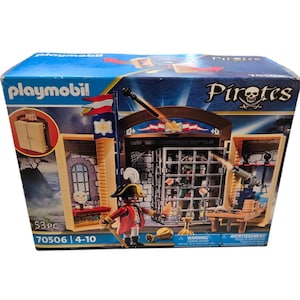May include: Playmobil Pirates playset in a blue box. The set includes a pirate figure, a jail, a cannon, and other accessories. The box has the text "Pirates" and "53 PC".