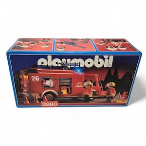 May include: A Playmobil toy set box showing a red fire engine with the number 26, a white hose, and two toy firefighters. The box has the Playmobil logo and the number 3880.