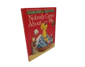 May include: A vintage Sesame Street "Nobody Cares About Me" book. The cover is red with the title in large white letters. Big Bird is illustrated in bed, wearing a nightcap and wrapped in a blue and white checkered blanket.