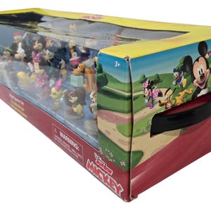 May include: A boxed set of Disney's Mickey Mouse Clubhouse figurines. The box is red and yellow with a clear plastic front, showcasing various character figures. The box art features Mickey, Minnie, Donald, and Goofy.