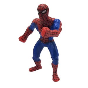 May include: A red, blue, and black Spider-Man action figure in a fighting pose. The figure has a red mask with white eyes, a red and black webbed suit, and blue accents. The figure is approximately 4 inches tall.