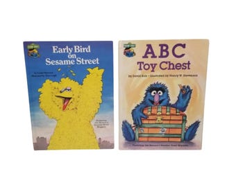 May include: Two vintage Sesame Street children's books. The book on the left is titled "Early Bird on Sesame Street" with a yellow Big Bird illustration. The book on the right is titled "ABC Toy Chest" with a blue monster illustration.