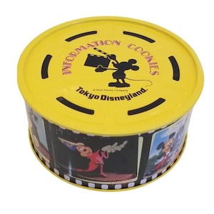 May include: A round yellow tin of "Information Cookies" from Tokyo Disneyland. The lid features Mickey Mouse holding a film clapper. The sides of the tin display cartoon images of Mickey Mouse. The tin is a souvenir.