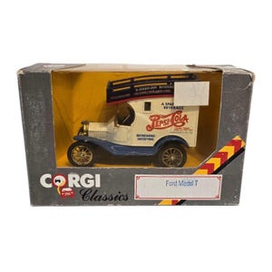 May include: A vintage Pepsi-Cola Ford Model T toy truck in its original box. The truck is white with blue accents and gold wheels, featuring Pepsi-Cola branding. The box is gray with the Corgi Classics logo.